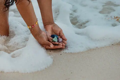 Manos ahuecadas sosteniendo cristales de los chakras mientras la espuma del mar las acaricia