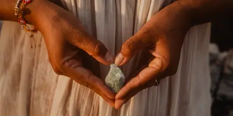 Manos formando un corazón alrededor de un cuarzo verde a la luz dorada del atardecer