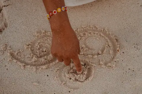 Un dedo traza una espiral en la arena, gesto de intención y apertura del ritual