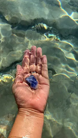 Una mano bajo el agua cristalina sostiene un cuarzo azul, entre reflejos de luz
