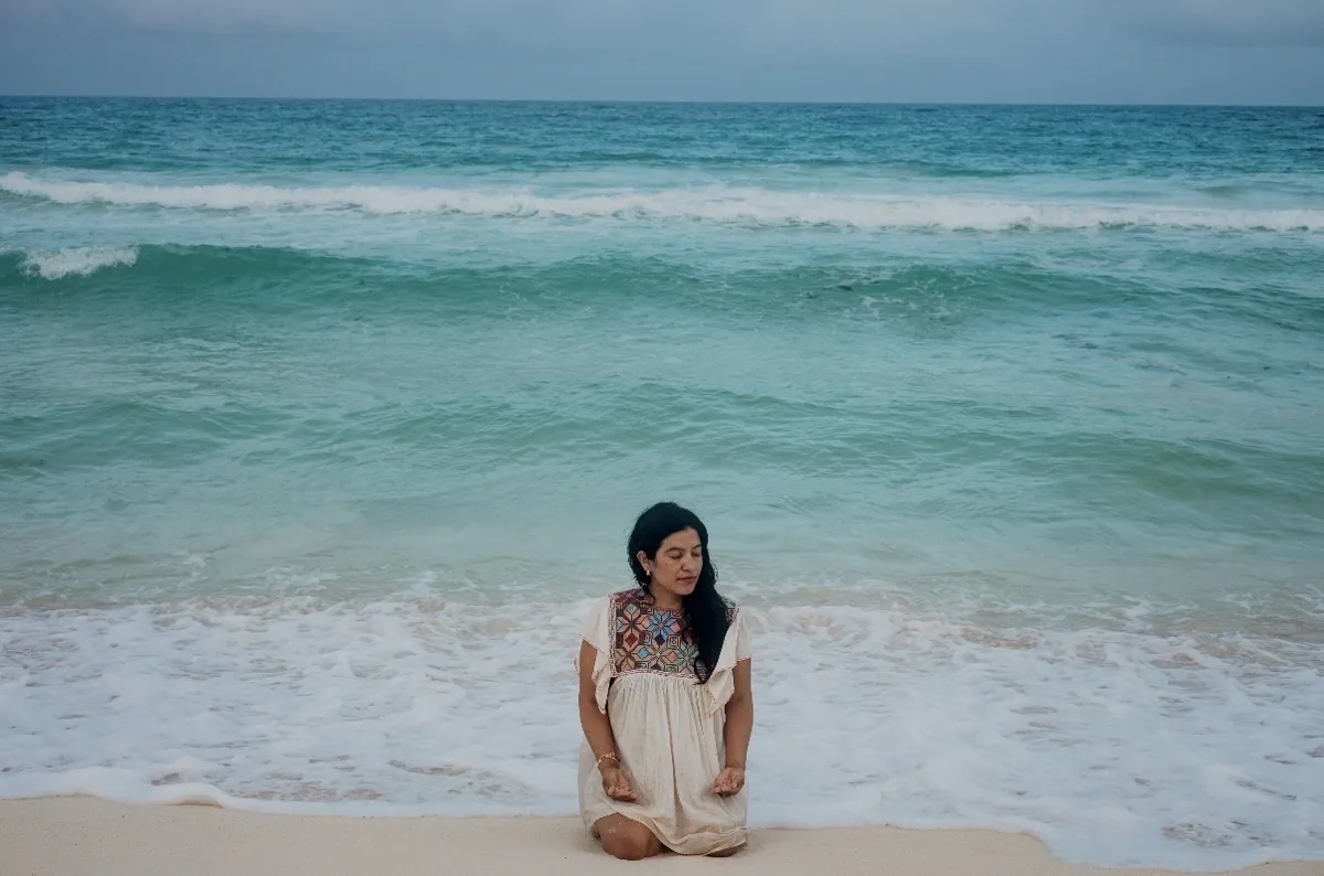Blanca Coutiño de espaldas mirando el mar, vestido de lino con bordado maya, en un momento de introspección y transición